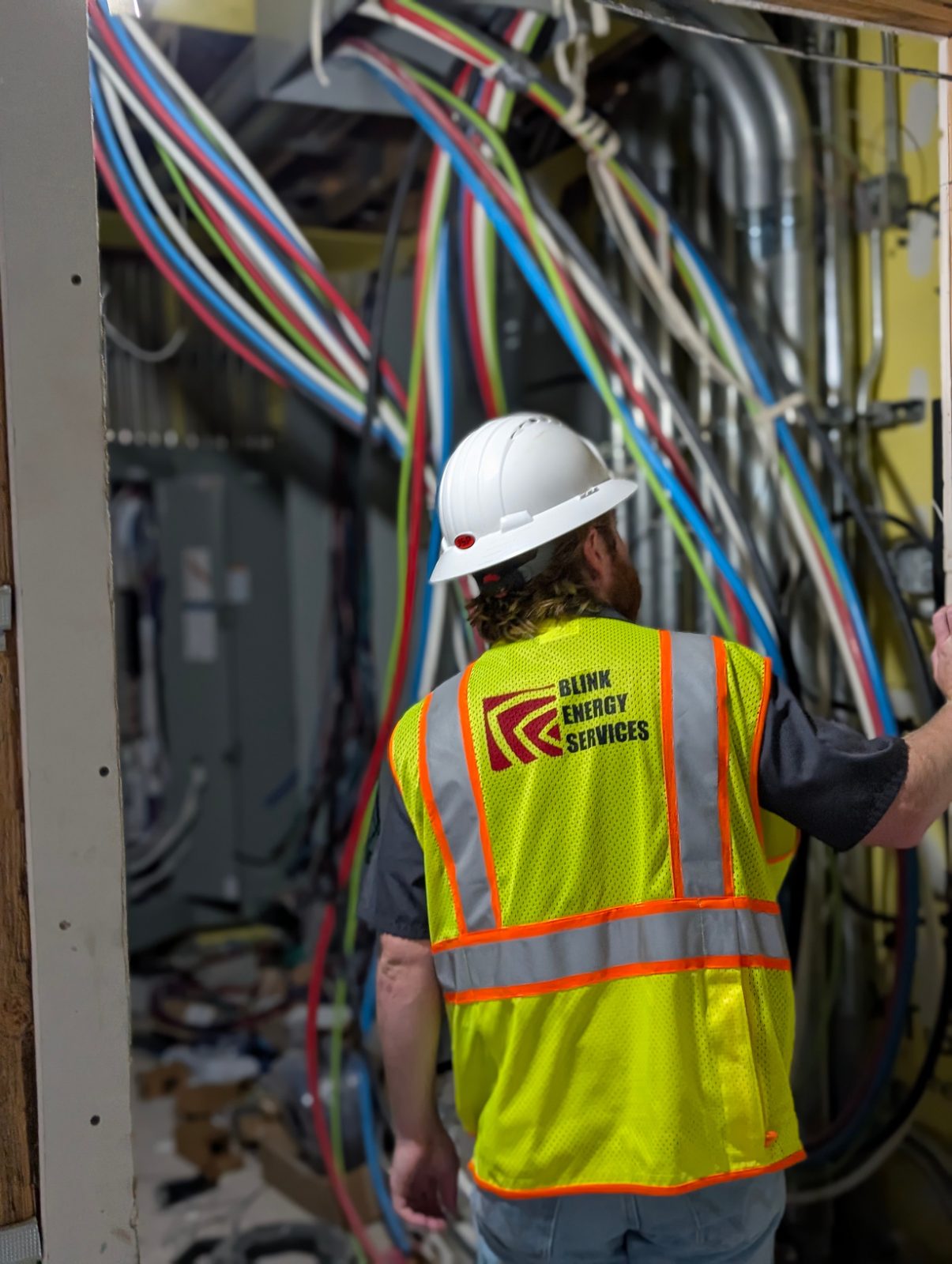 A Blink Energy Services technician in a hard hat and safety vest inspects electrical and mechanical lines during construction.