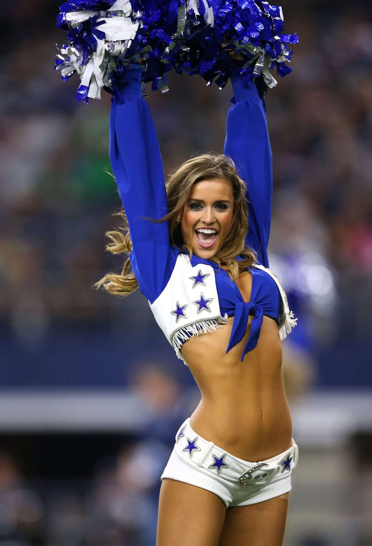 Dallas Cowboys Cheerleader with pom-poms raised in the stadium