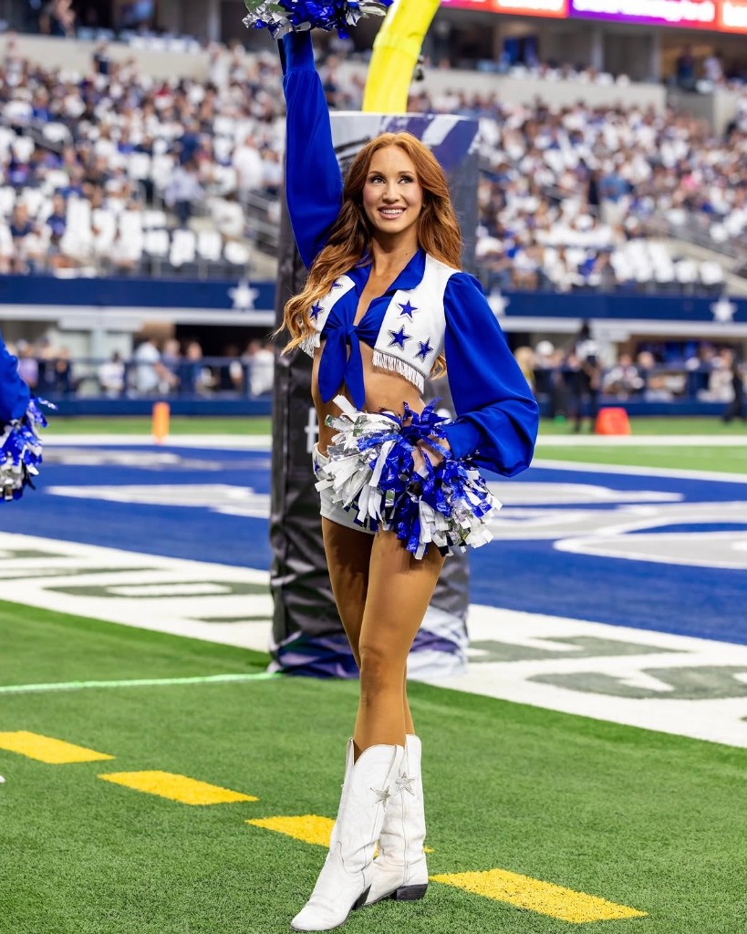 Dallas Cowboys Cheerleader with red hair and pom-poms on the field