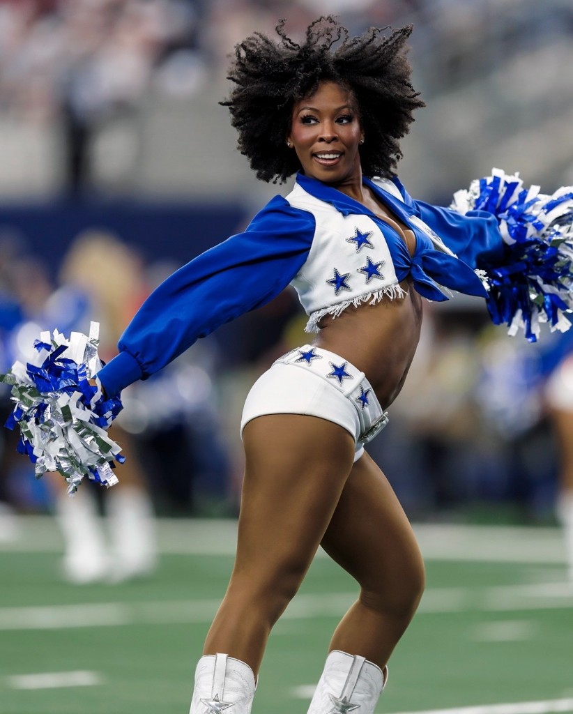 Dallas Cowboys Cheerleader with natural curls and pom-poms on the field